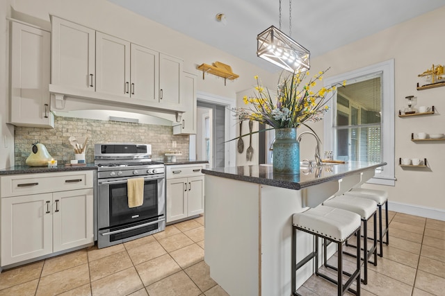 kitchen featuring stainless steel gas stove, hanging light fixtures, an island with sink, white cabinets, and a kitchen bar