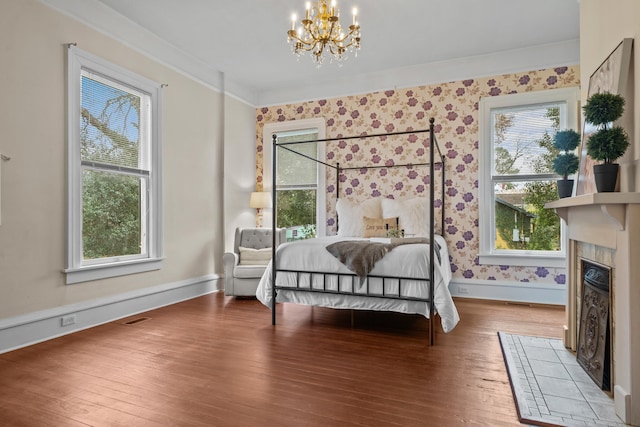 bedroom with hardwood / wood-style flooring, a fireplace, ornamental molding, and a chandelier