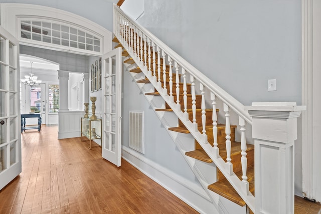 stairway with an inviting chandelier, hardwood / wood-style floors, decorative columns, and french doors