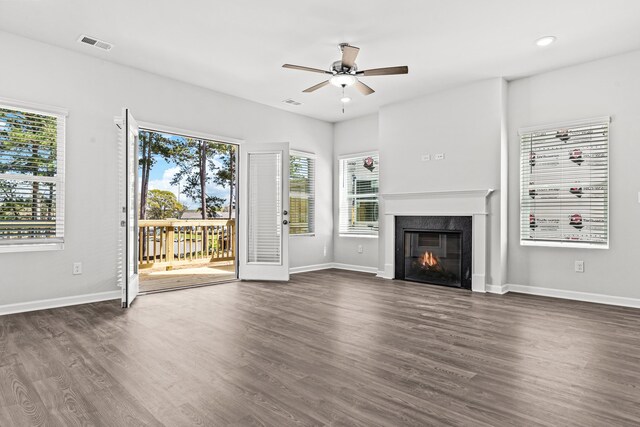 unfurnished living room featuring ceiling fan, a premium fireplace, dark hardwood / wood-style flooring, and a wealth of natural light