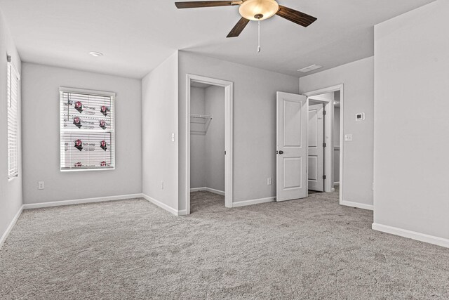 unfurnished bedroom with a walk in closet, light colored carpet, a closet, and ceiling fan