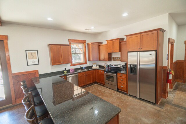 kitchen featuring a breakfast bar, kitchen peninsula, dark stone counters, and appliances with stainless steel finishes