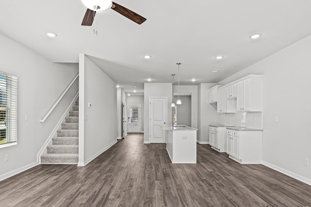 kitchen with decorative light fixtures, white cabinets, backsplash, dark wood-type flooring, and a center island with sink