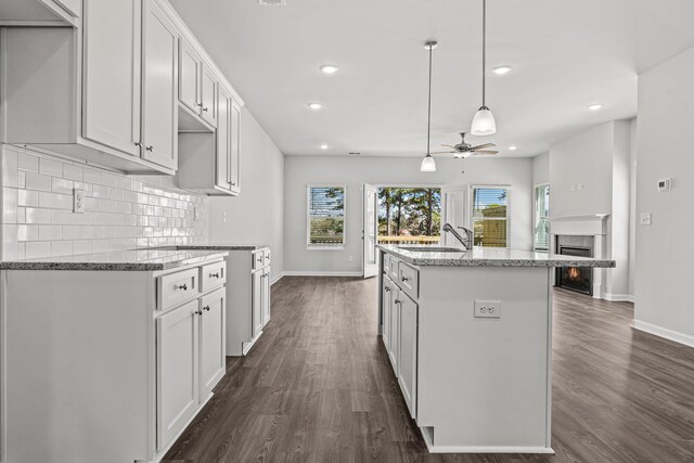 kitchen featuring white cabinetry, light stone countertops, an island with sink, and hanging light fixtures