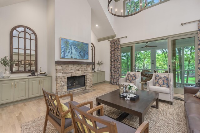 living room with a stone fireplace, light wood-type flooring, a notable chandelier, and high vaulted ceiling