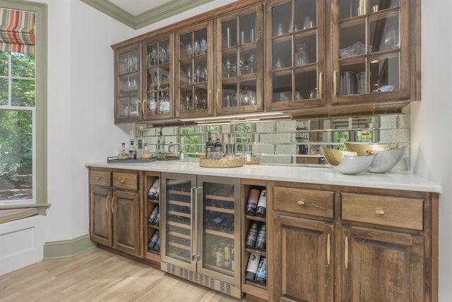 bar with tasteful backsplash, crown molding, dark brown cabinetry, and light wood-type flooring