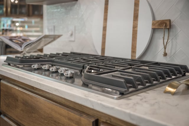 details with decorative backsplash, range hood, and stainless steel gas cooktop