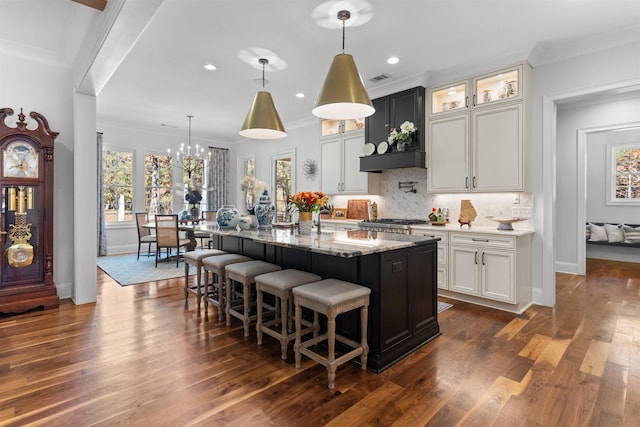 kitchen featuring white cabinetry, decorative light fixtures, custom exhaust hood, and an island with sink