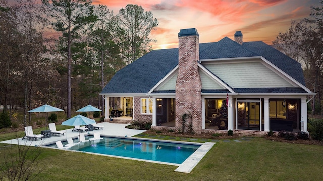 back house at dusk with a patio area and a lawn