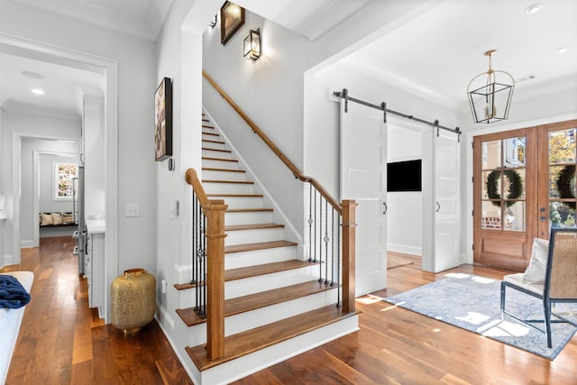 foyer with crown molding, a barn door, a chandelier, and hardwood / wood-style floors