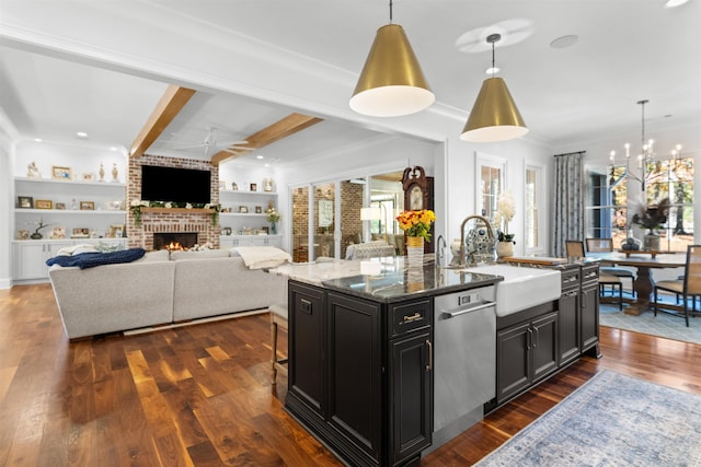 kitchen featuring decorative light fixtures, sink, dark stone countertops, stainless steel dishwasher, and a center island with sink