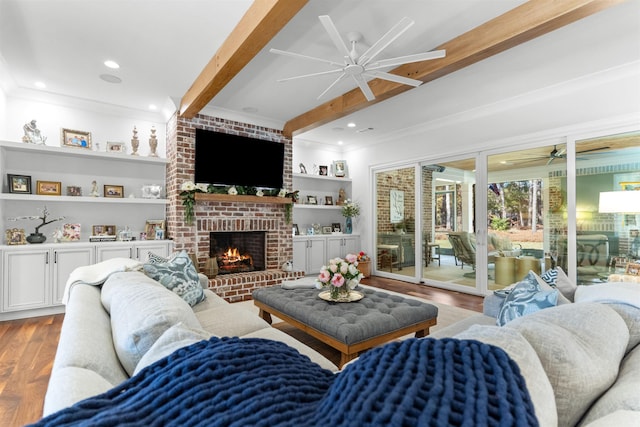 living room with ceiling fan, hardwood / wood-style floors, ornamental molding, a brick fireplace, and beamed ceiling