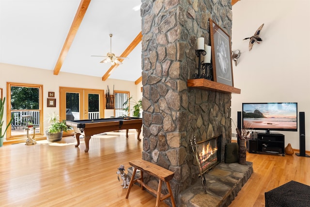 living room with light hardwood / wood-style flooring, ceiling fan, a stone fireplace, french doors, and beamed ceiling