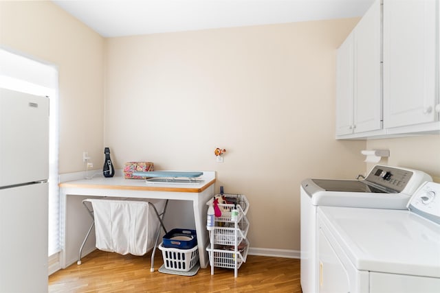 clothes washing area featuring cabinets, washer and clothes dryer, and light hardwood / wood-style floors