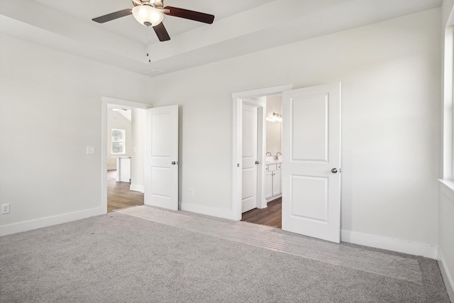 unfurnished bedroom with dark carpet, a raised ceiling, and ensuite bathroom