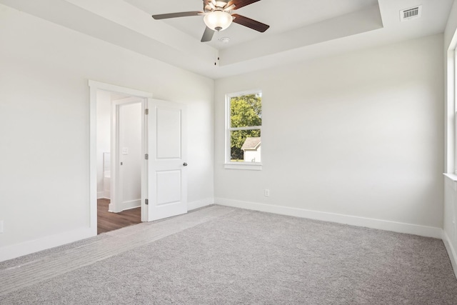 carpeted spare room with ceiling fan and a raised ceiling