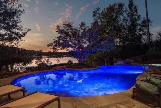 pool at dusk with a water view and an in ground hot tub