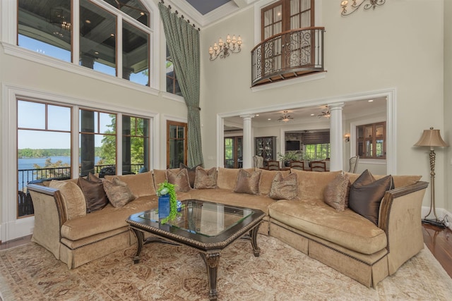 living room with ornate columns, a towering ceiling, hardwood / wood-style floors, crown molding, and a water view