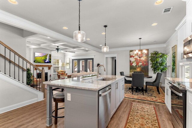 kitchen featuring light stone counters, stainless steel appliances, an island with sink, and white cabinets