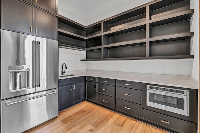 kitchen with open shelves, appliances with stainless steel finishes, a sink, light countertops, and light wood-style floors