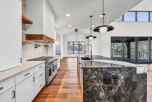 kitchen featuring white cabinets, decorative light fixtures, custom range hood, appliances with stainless steel finishes, and a sink