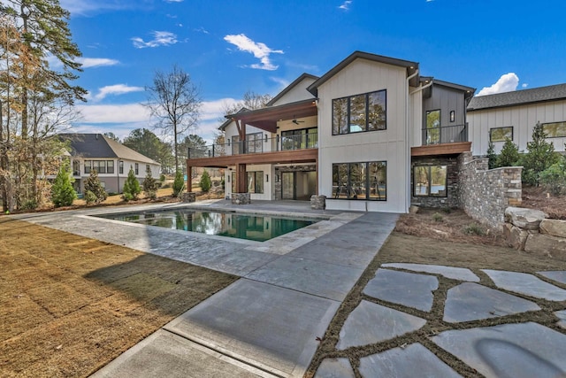 back of property with a patio area, an outdoor pool, a balcony, and a ceiling fan