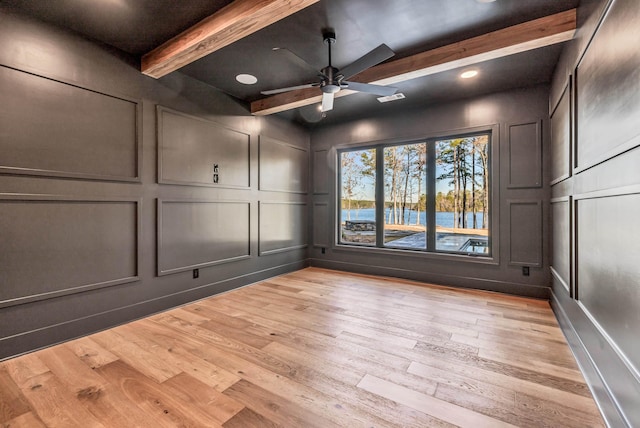 unfurnished room featuring ceiling fan, light wood finished floors, a decorative wall, and beamed ceiling