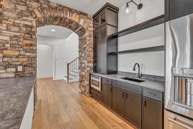 kitchen with dark brown cabinets, open shelves, stainless steel appliances, a sink, and arched walkways