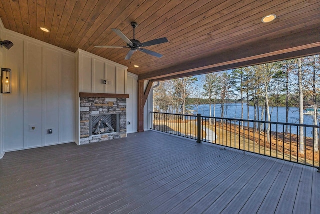 wooden terrace with ceiling fan, a stone fireplace, and a water view