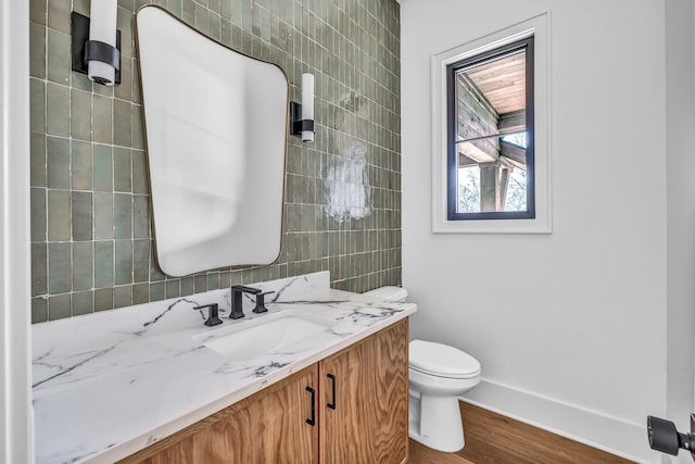 half bathroom with baseboards, toilet, tile walls, vanity, and wood finished floors