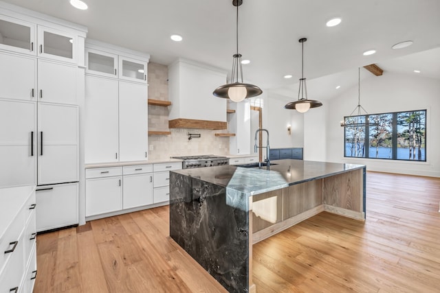 kitchen with glass insert cabinets, a kitchen island with sink, white cabinets, and a sink