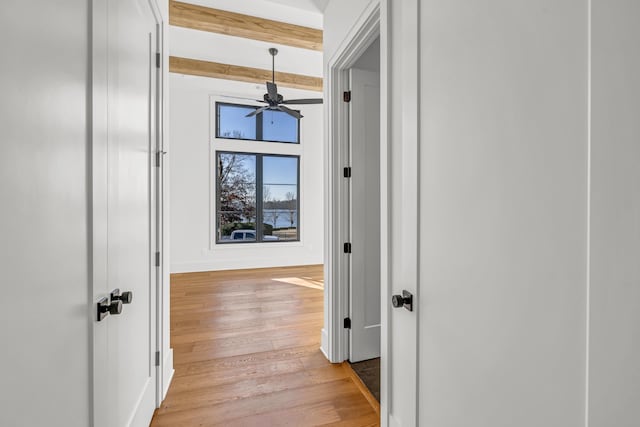 hallway featuring light wood finished floors, baseboards, and beam ceiling