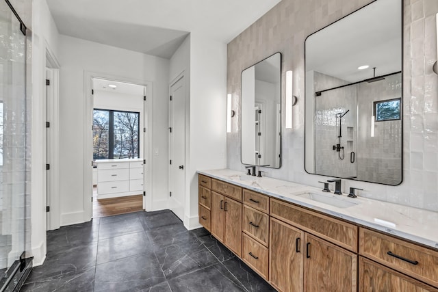 full bathroom with a shower stall, double vanity, baseboards, and a sink