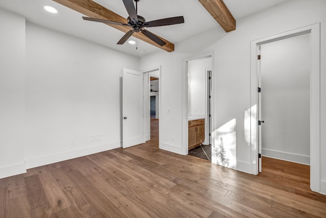 unfurnished bedroom with dark wood-style flooring, baseboards, a walk in closet, beamed ceiling, and recessed lighting