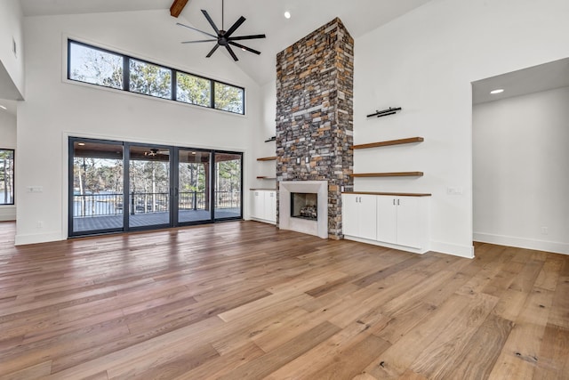 unfurnished living room with light wood finished floors, baseboards, a stone fireplace, and a ceiling fan