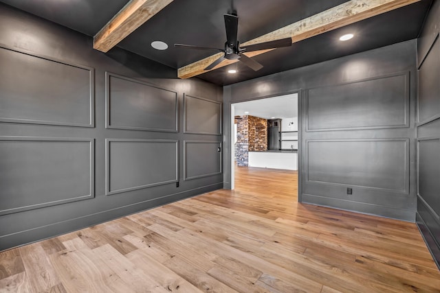 unfurnished room featuring a decorative wall, light wood-type flooring, a ceiling fan, and beam ceiling