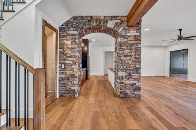 corridor with baseboards, stairs, beamed ceiling, light wood-style flooring, and arched walkways