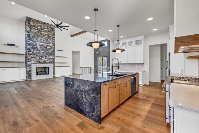 kitchen featuring glass insert cabinets, dark stone counters, white cabinetry, a center island with sink, and a sink