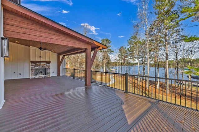 wooden terrace featuring a water view, a stone fireplace, and a ceiling fan