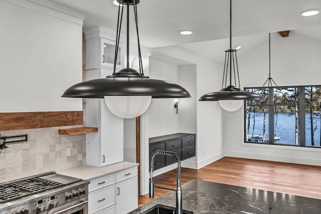 kitchen with white cabinets, baseboards, light wood-style flooring, decorative backsplash, and high end stove