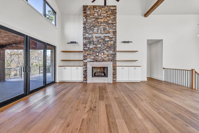 unfurnished living room with ceiling fan, a stone fireplace, light wood-type flooring, beam ceiling, and high vaulted ceiling