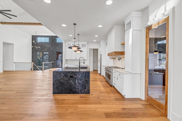 kitchen with a kitchen island with sink, pendant lighting, white cabinets, light wood-style flooring, and high end stainless steel range oven