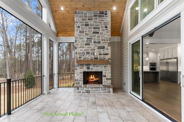 unfurnished sunroom featuring wood ceiling, an outdoor stone fireplace, and vaulted ceiling