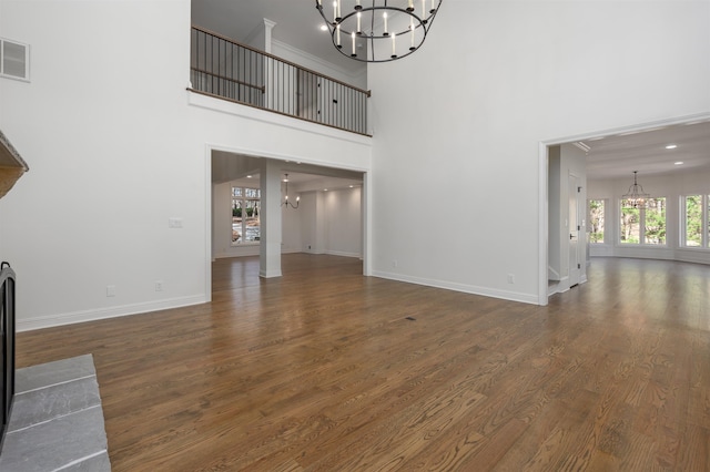 unfurnished living room with wood finished floors, baseboards, visible vents, an inviting chandelier, and a high ceiling