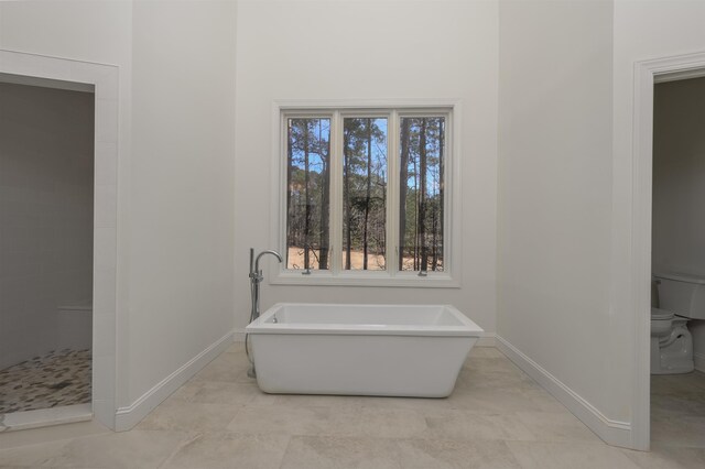 bathroom with toilet, tiled shower, baseboards, and a freestanding bath