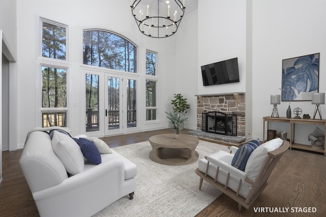 living room with baseboards, a notable chandelier, a stone fireplace, and wood finished floors