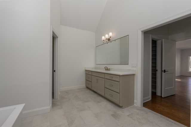 bathroom with a washtub, baseboards, vanity, and vaulted ceiling