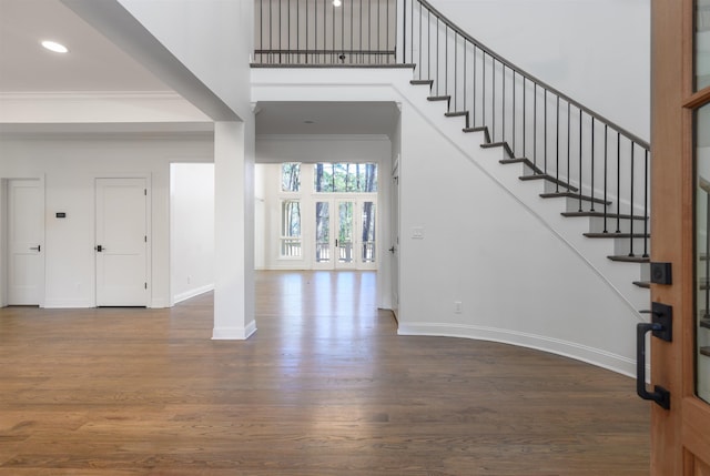 foyer entrance with wood finished floors, stairway, crown molding, baseboards, and a towering ceiling