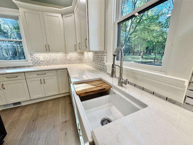 kitchen with sink, decorative backsplash, white cabinets, and light wood-type flooring