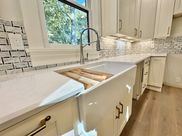 kitchen with white cabinetry, light stone countertops, light hardwood / wood-style floors, and decorative backsplash